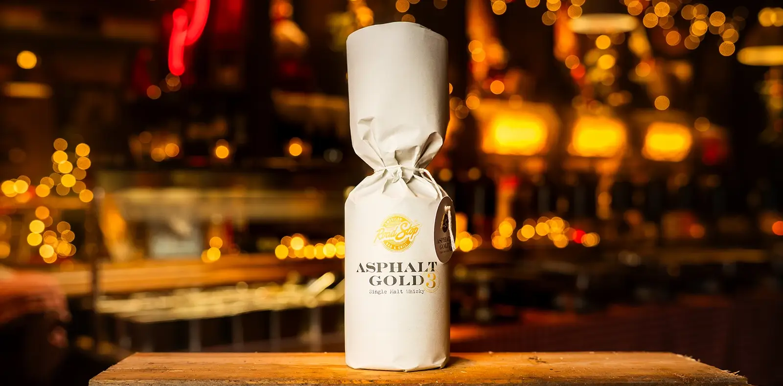 Whiskyflasche mit Packagingdesign „Asphalt Gold“ auf rustikalem Setting mit warmem Licht
