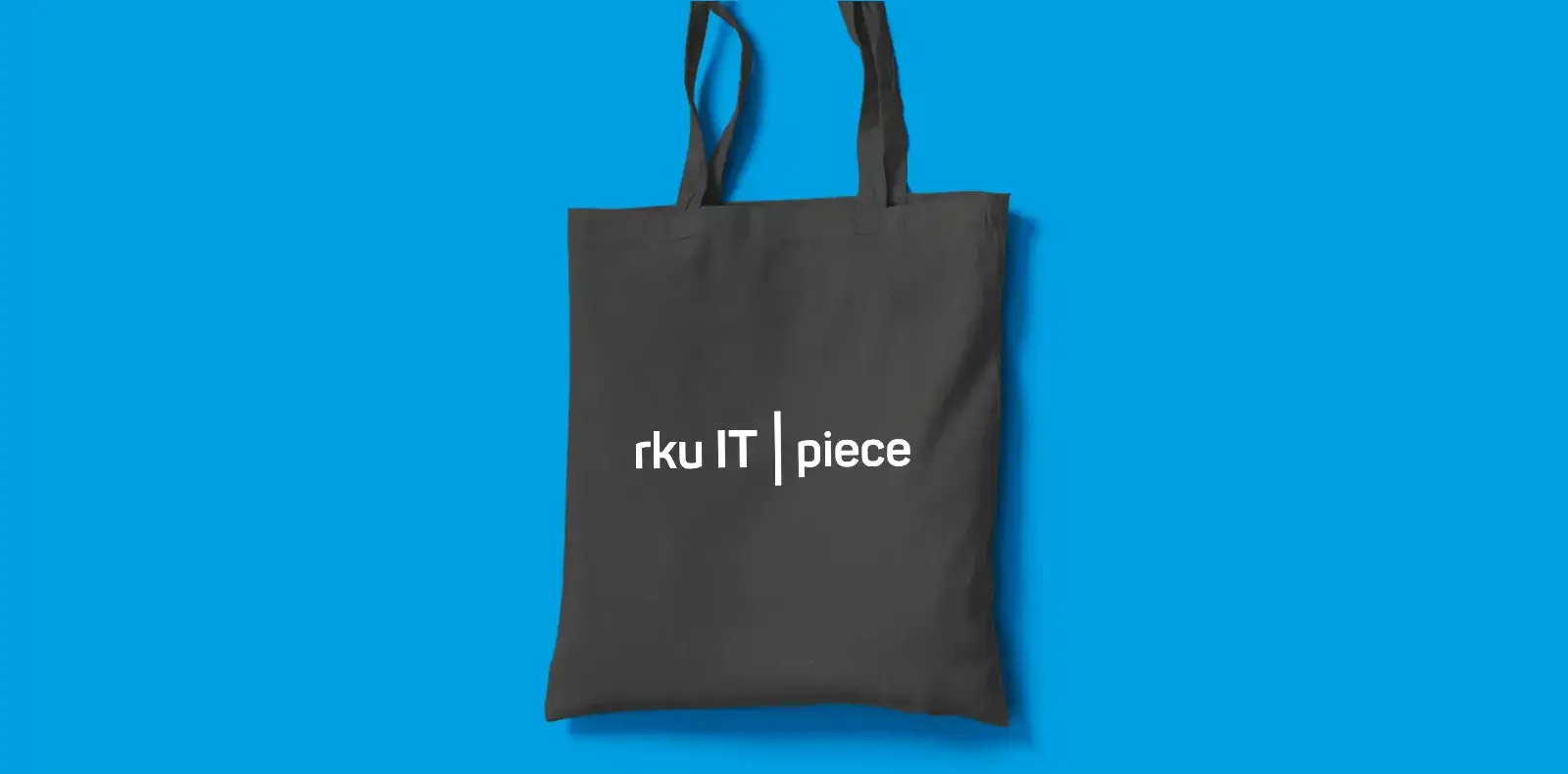 Schwarze Stofftasche mit „rku IT piece“ Logo auf blauem Hintergrund