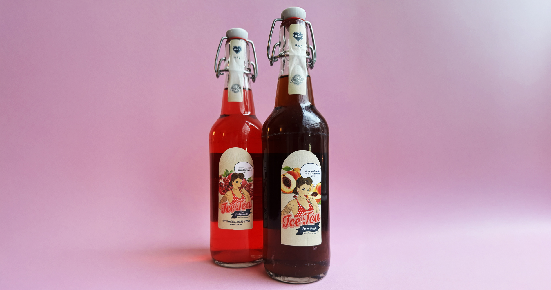 Zwei Glasflaschen mit Ice-Tea-Labels vor rosafarbenem Hintergrund