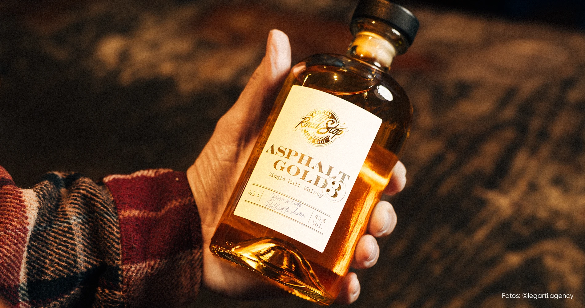 Hand hält Whiskyflasche mit Packagingdesign in natürlicher Umgebung