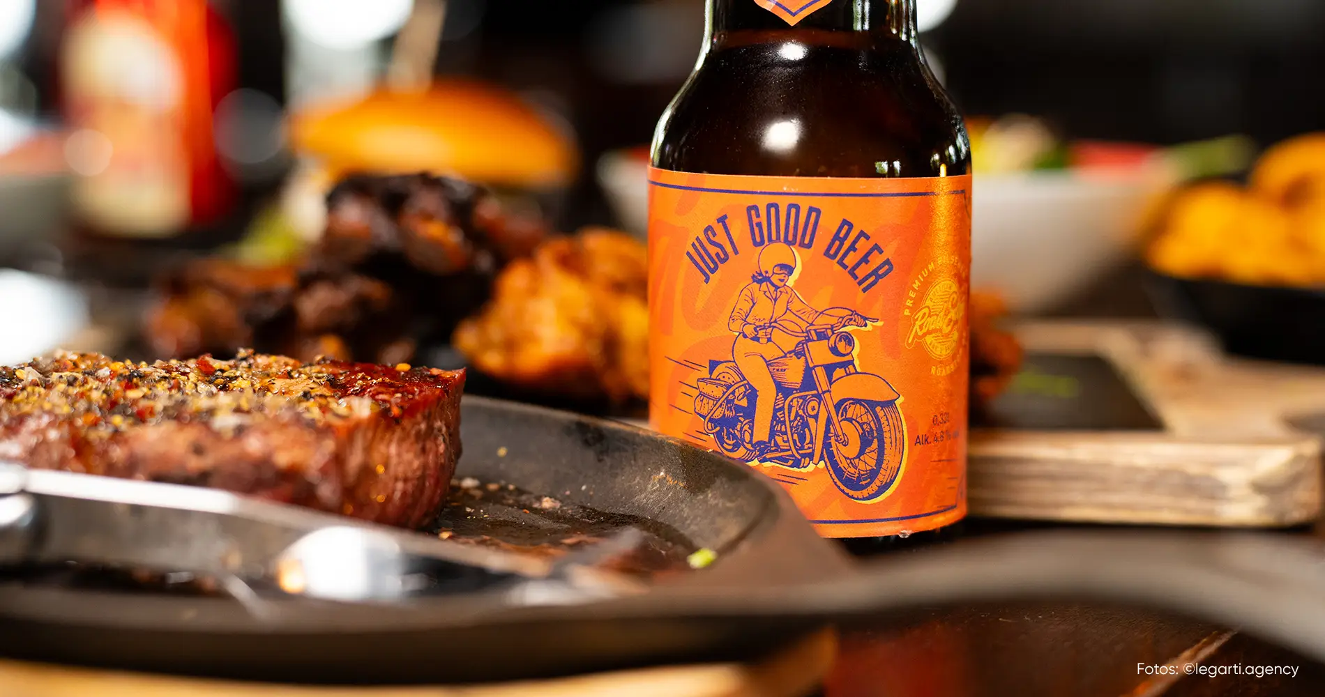 Bierflasche mit auffälligem Retro-Label neben gegrilltem Steak auf einem Tisch