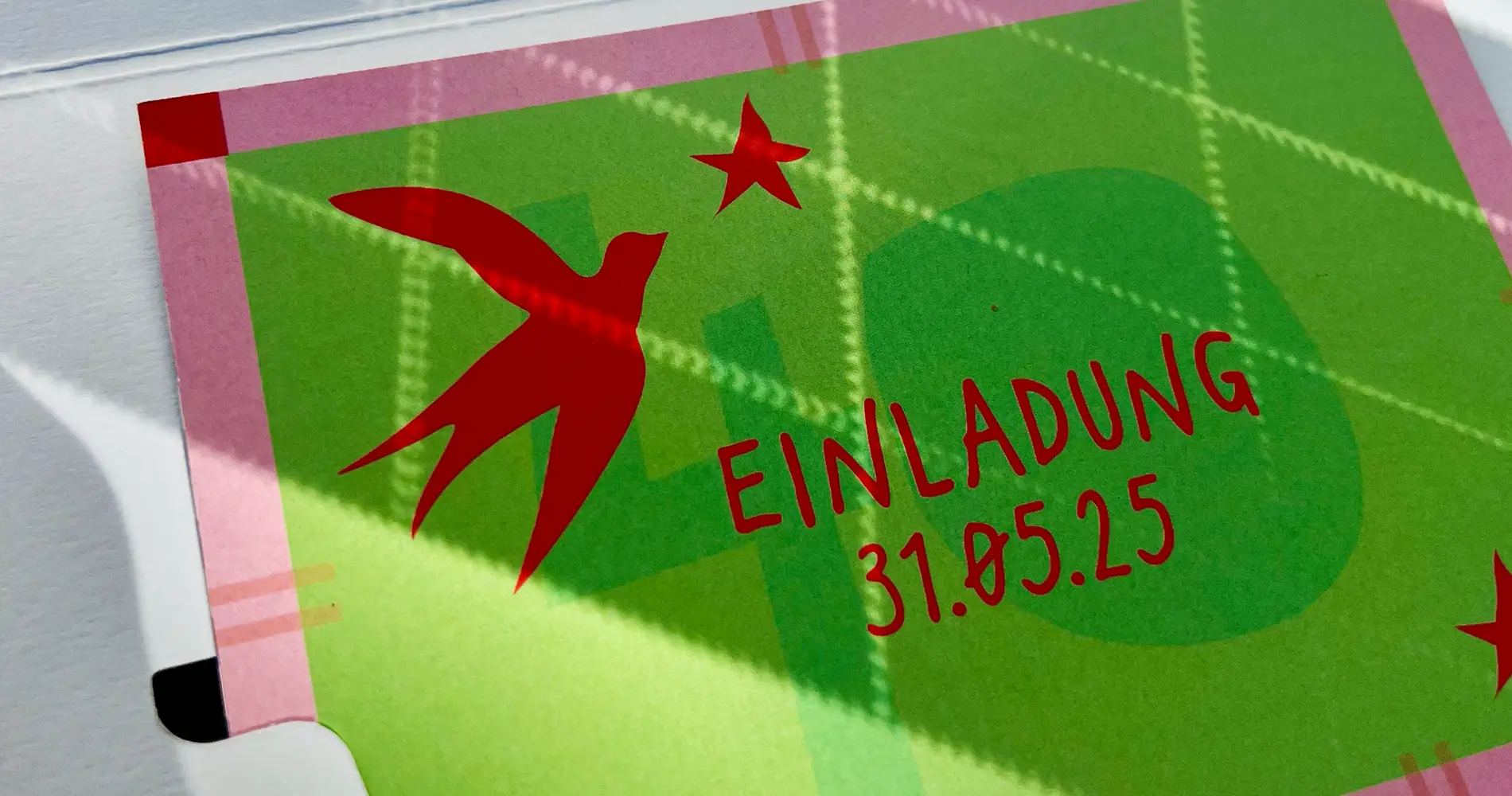 Detail einer Einladungskarte mit roter Typografie „Einladung 31.05.25“ und illustrativem Vogel auf grünem Hintergrund