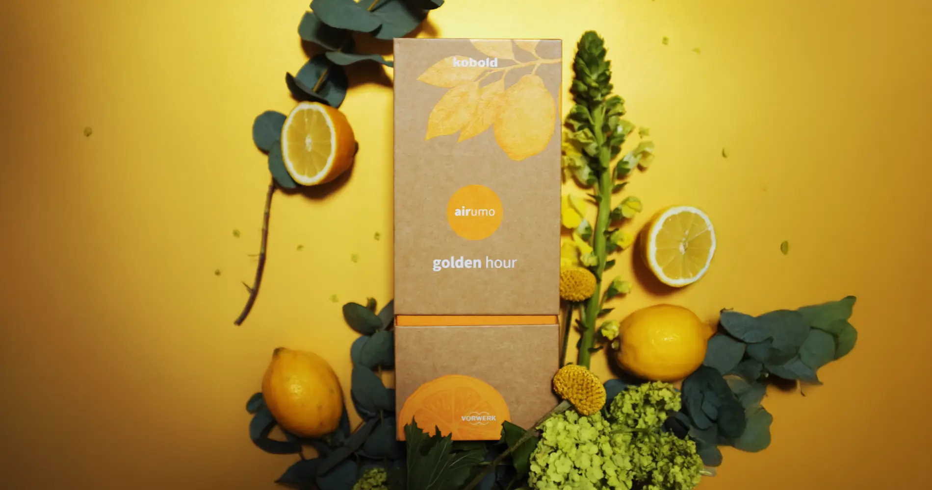 Produktinszenierung des Kobold Airumo Dufts „Golden Hour“ mit Verpackung, Zitronen und Pflanzen in gelber Farbwelt