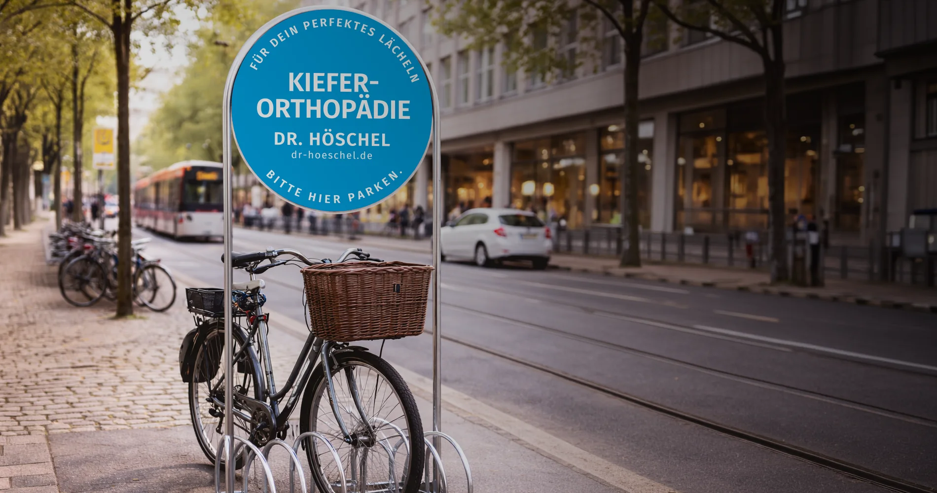 Fahrradständer mit Werbeschild für Dr. Höschel Kieferorthopädie im Stadtraum, Fahrrad im Vordergrund