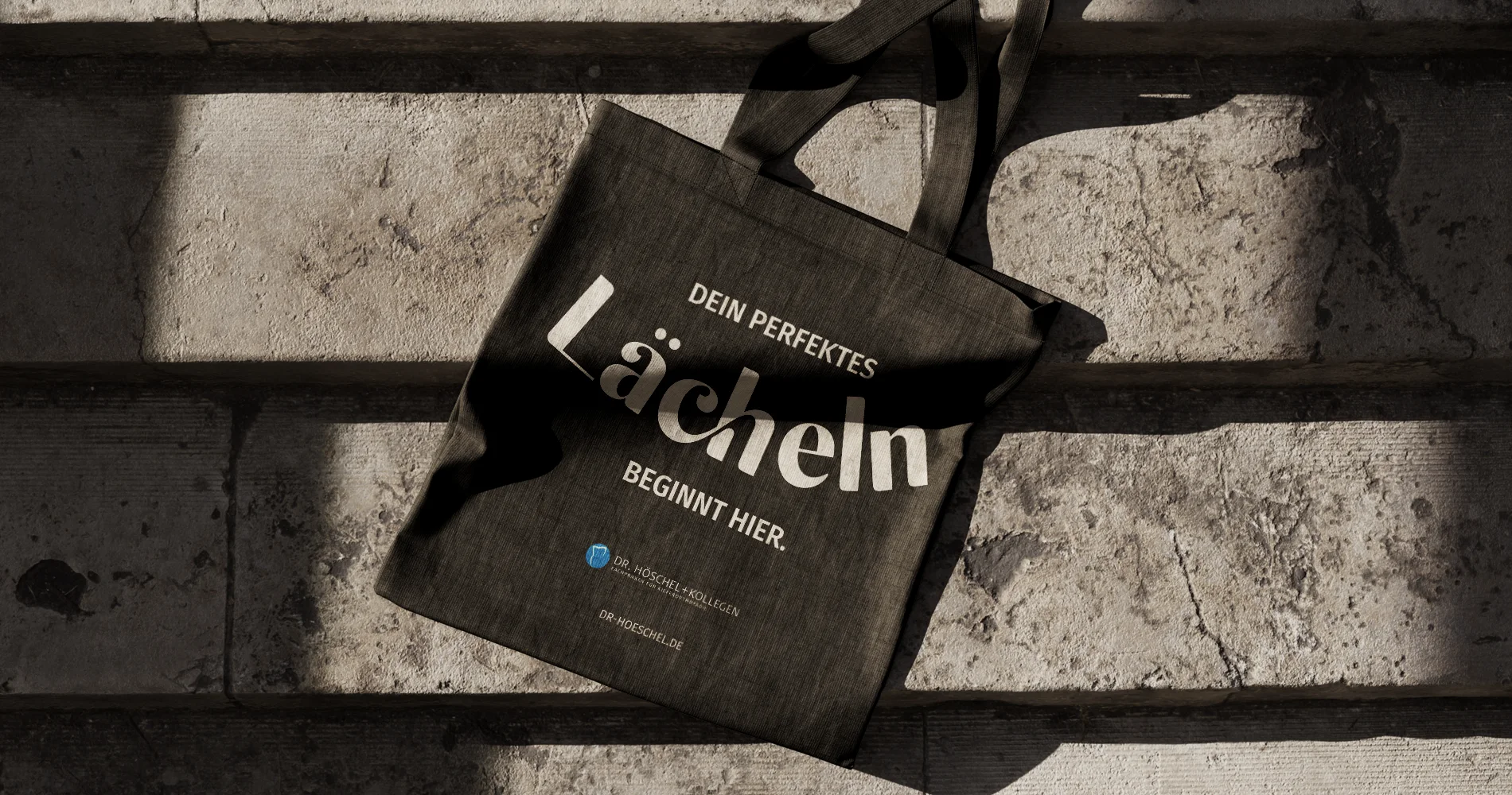 Stofftasche mit Aufdruck „Dein perfektes Lächeln beginnt hier“ von Dr. Höschel & Kollegen, an Treppe liegend