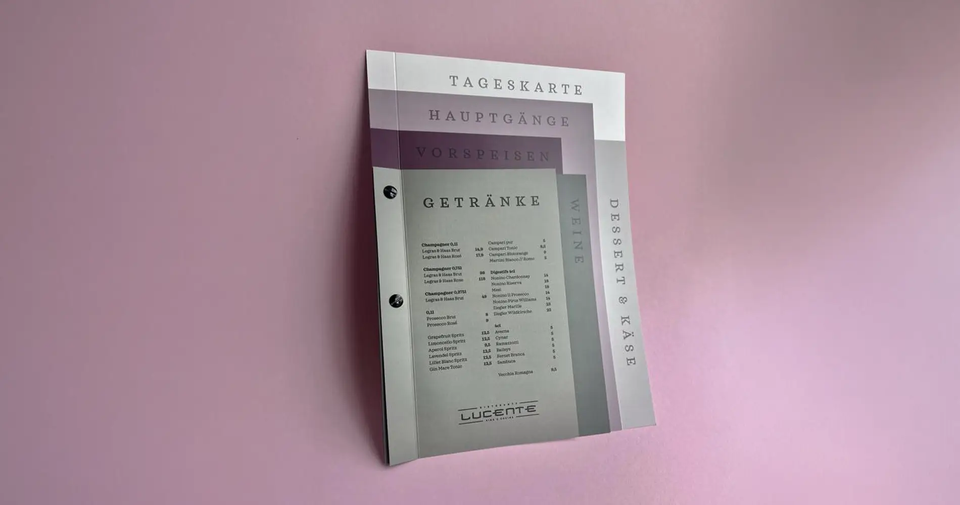 Fotografie einer aufgefächerten Speisekarte mit Registertabs für Getränke, Vorspeisen und Hauptgänge vor rosafarbenem Hintergrund