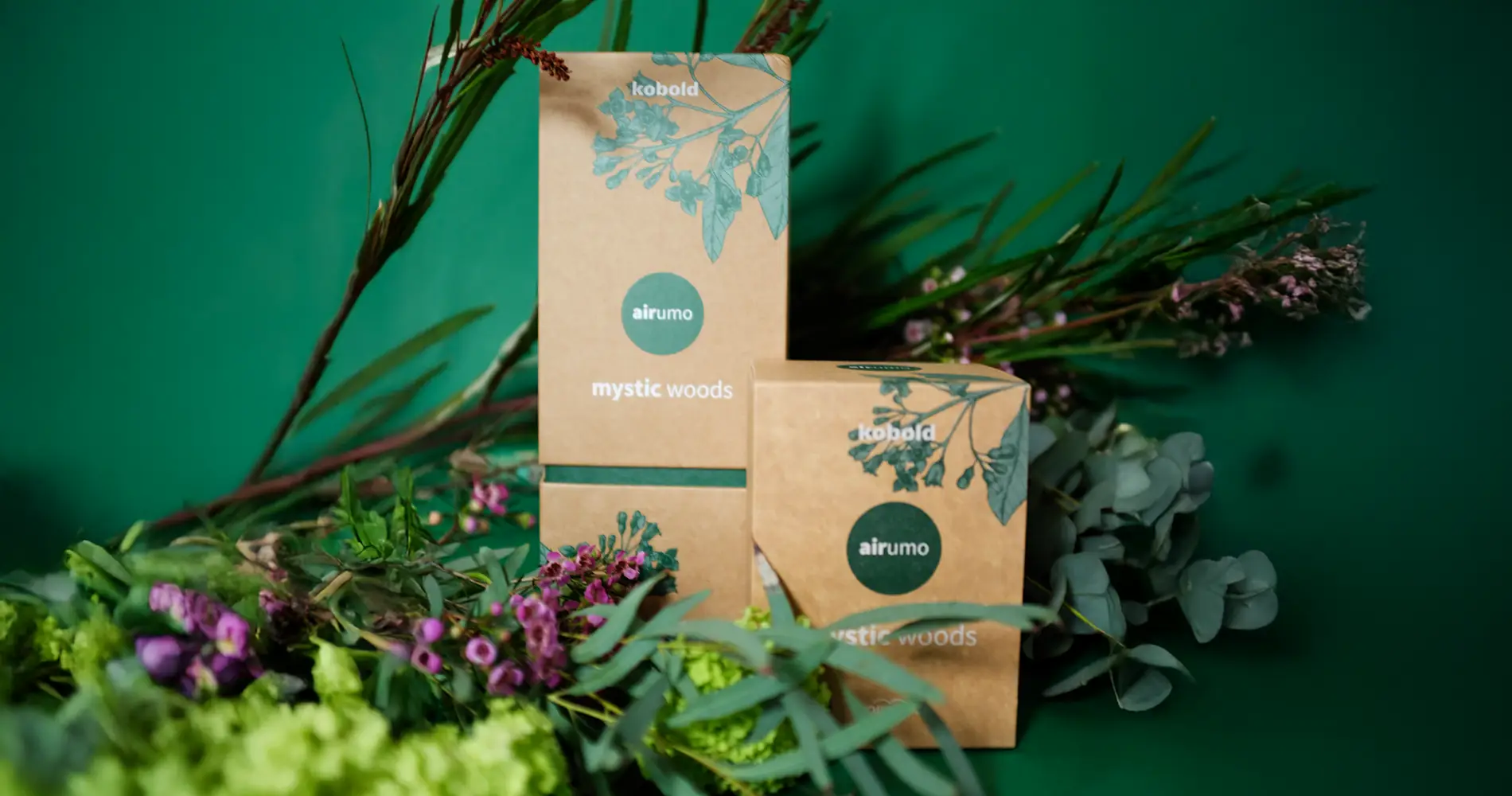 Produktinszenierung des Kobold Airumo Dufts „Mystic Woods“ mit Verpackung und natürlichen Pflanzen in grüner Farbwelt