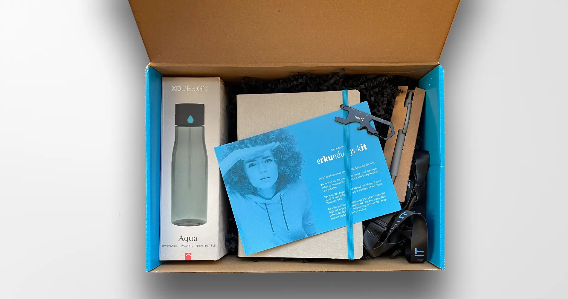 Inhalt einer Onboarding-Box für rku IT mit Notizbuch, Giveaways und Markenelementen