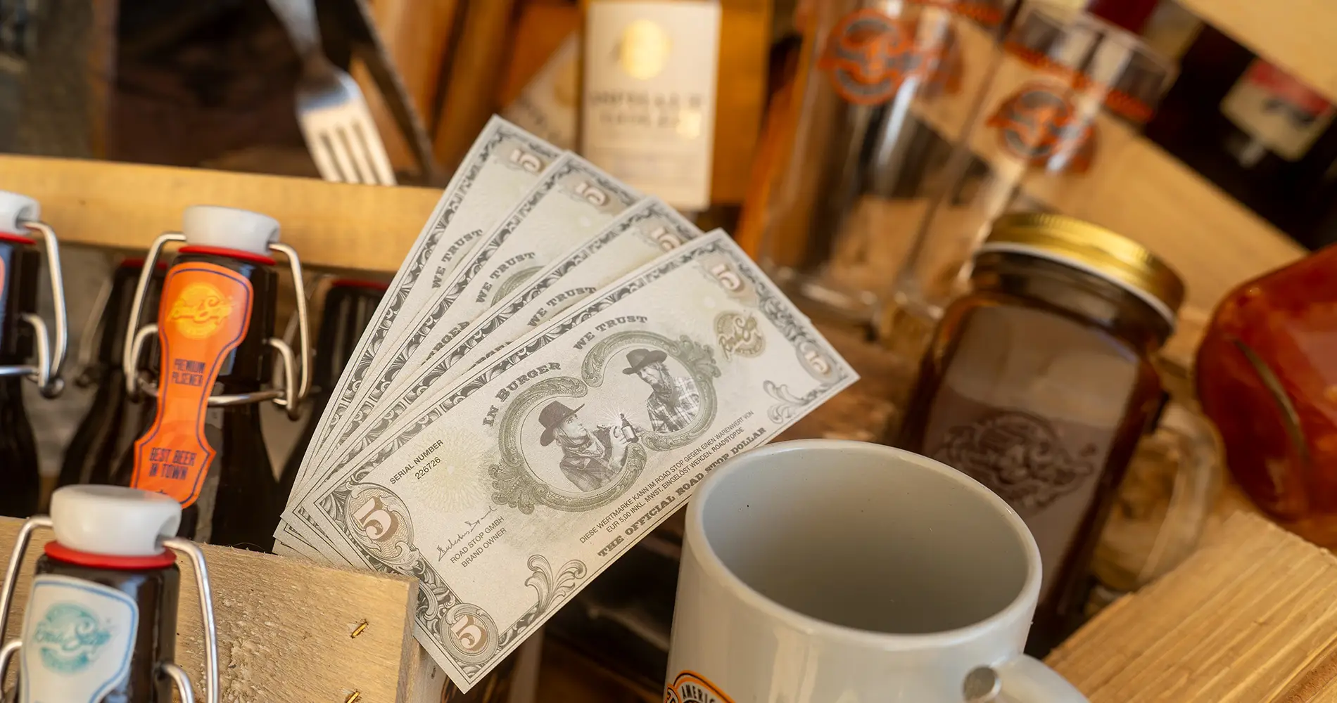 Detailaufnahme von amerikanisch inspirierter Gastronomie mit Dollarscheinen, Getränken und Dekoelementen im Road Stop Restaurant
