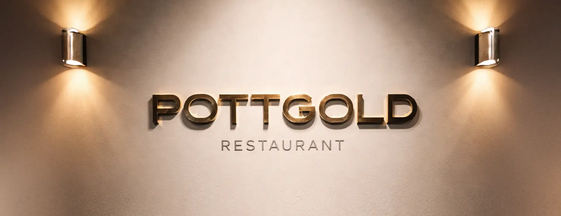 Wandbeschriftung „Pottgold Restaurant“ in goldener 3D-Typografie, beleuchtet durch zwei Wandleuchten