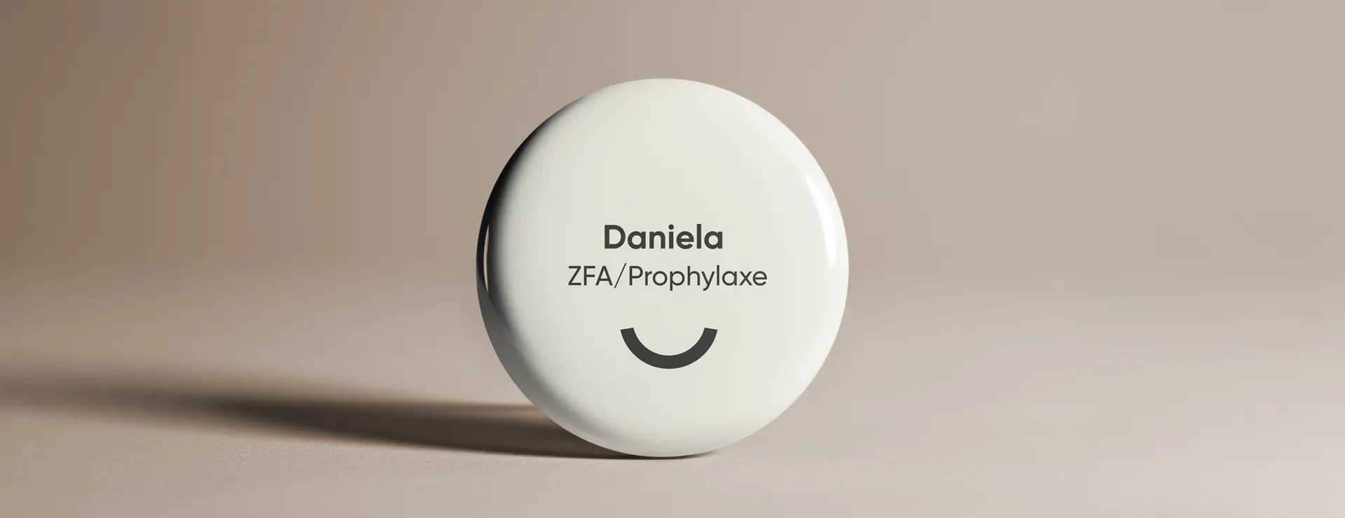 Namensschild mit der Aufschrift „Daniela, ZFA/Prophylaxe“ und stilisiertem Smiley