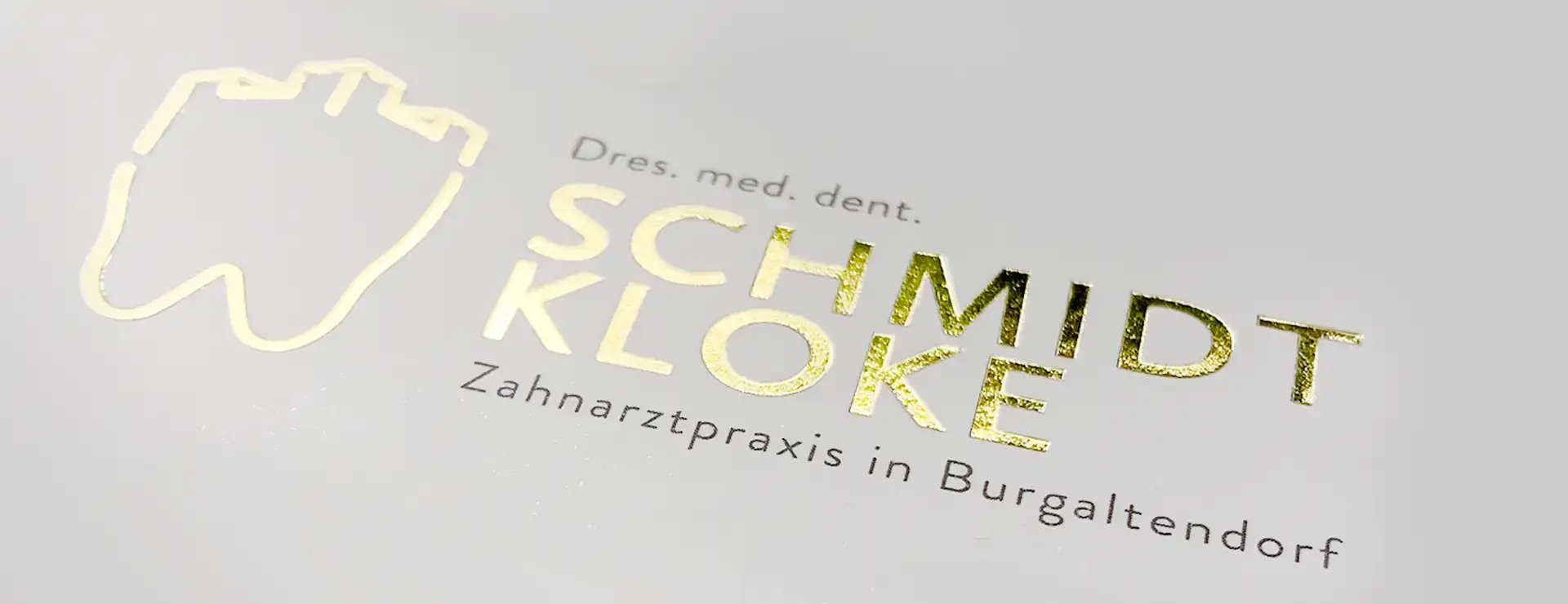 Logo der Zahnarztpraxis Schmidt & Kloke mit goldener Veredelung im Detail