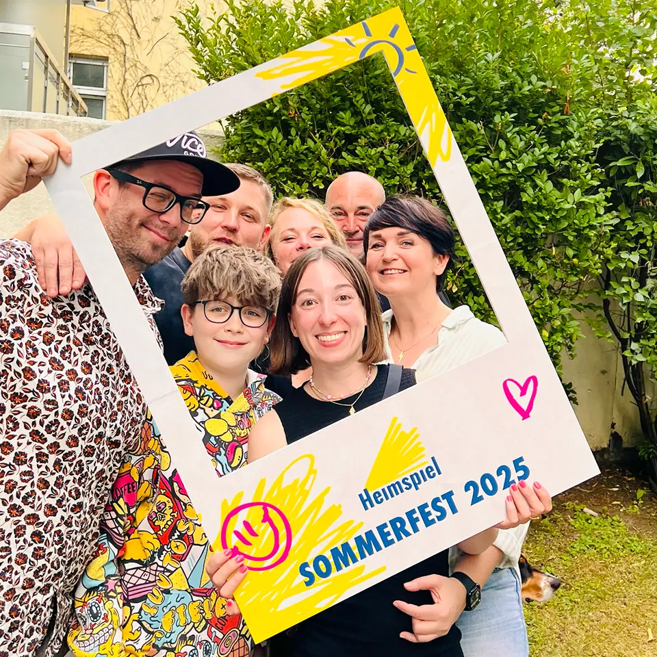 Gruppe von Menschen macht ein Selfie durch einen Rahmen beim Sommerfest Heimspiel 2025